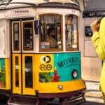 Una mujer frente a un tranvía en Portugal con una de las nuevas mochilas de viaje de Binnari haciendo un juego de contrastes de colores entre amarillo y verde.