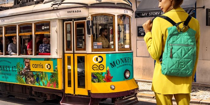 Una mujer frente a un tranvía en Portugal con una de las nuevas mochilas de viaje de Binnari haciendo un juego de contrastes de colores entre amarillo y verde.