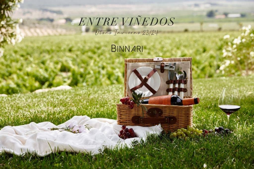 Cesta de pícnic con sábana blanca y copa de vino en un paraje entre viñedos.