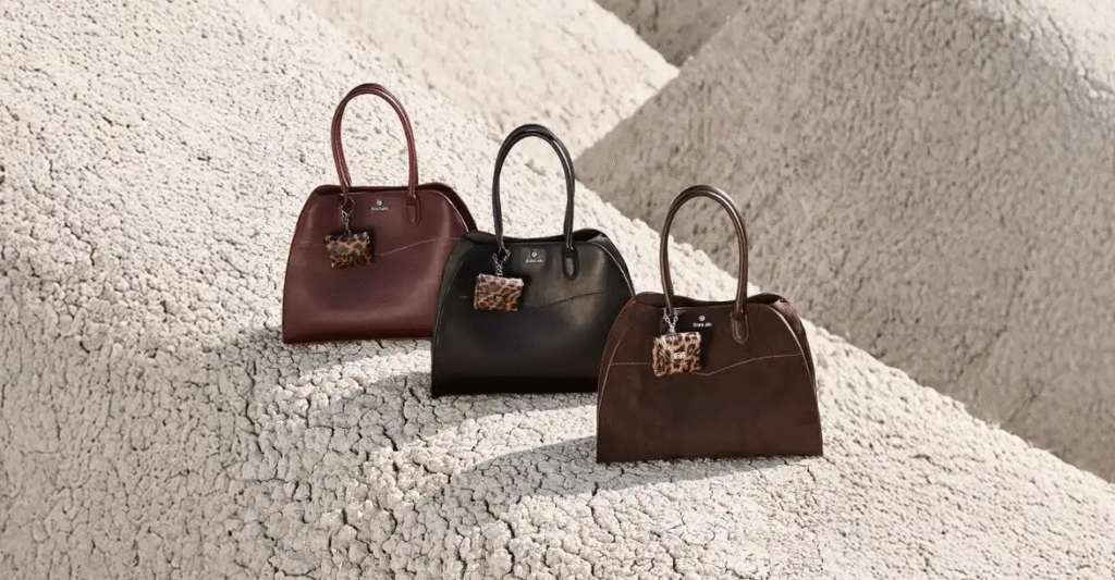 res bolsos otoño-invierno en tonos burdeos, negro y marrón con llaveros de estampado animal, fotografiados sobre un paisaje de tierra agrietada en tonos beige